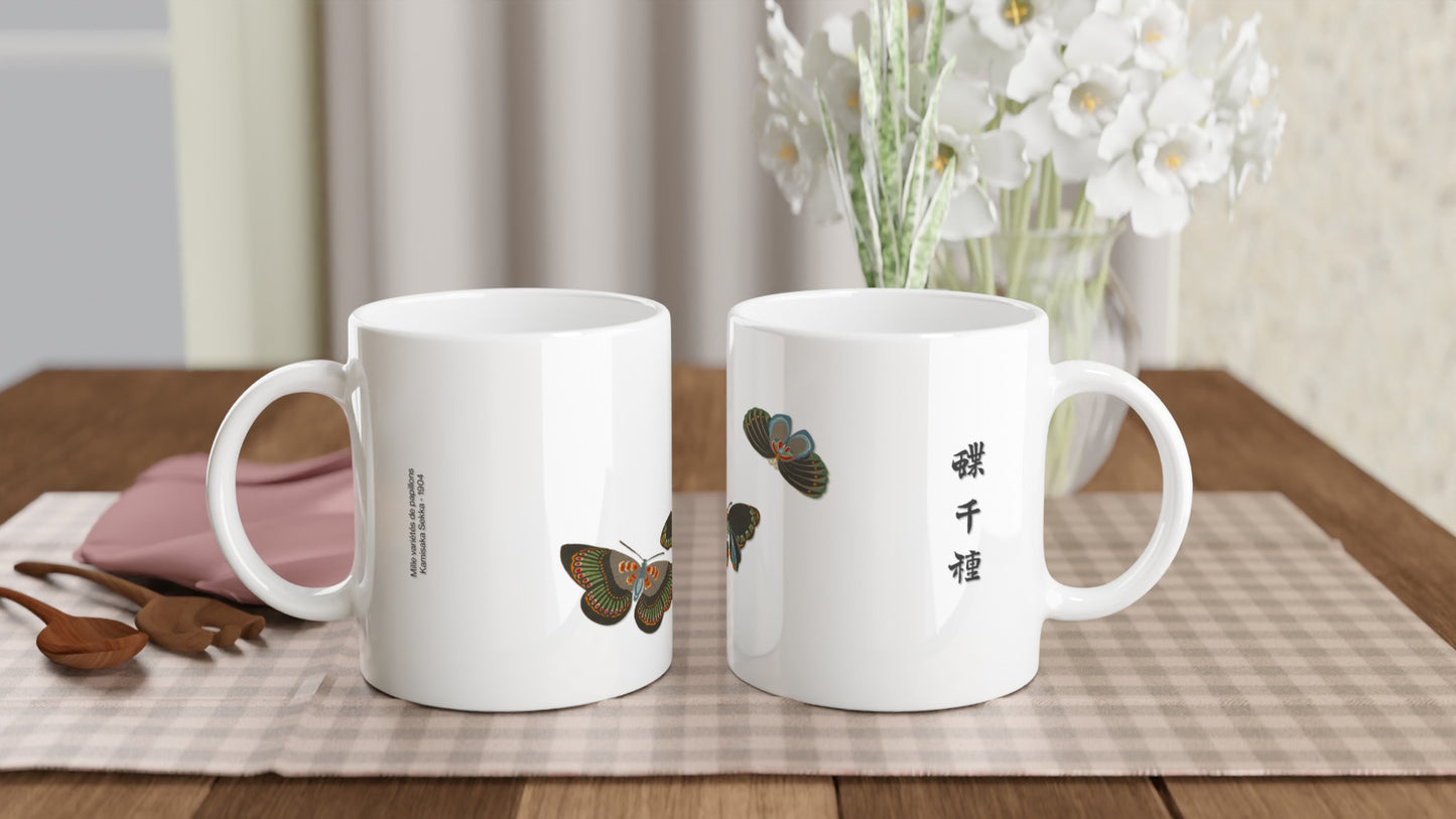 Planche de papillons aux motifs bleus et noirs – Kamisaka Sekka. Tasse blanche ornée de deux papillons stylisés aux ailes bleues et noires, avec des accents orangés et verts, et des inscriptions japonaises. Image d'illustration 2