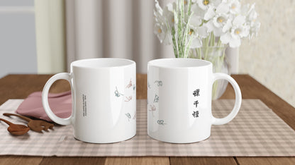Mug estampe de papillons rose pâle et bleu-gris, Kamisaka Sekka. Mug blanc décoré de papillons aux traits fins, de couleur rose pâle et bleu-gris, disposés en volée, avec des caractères japonais noirs sur le côté. Image d'illustration 2