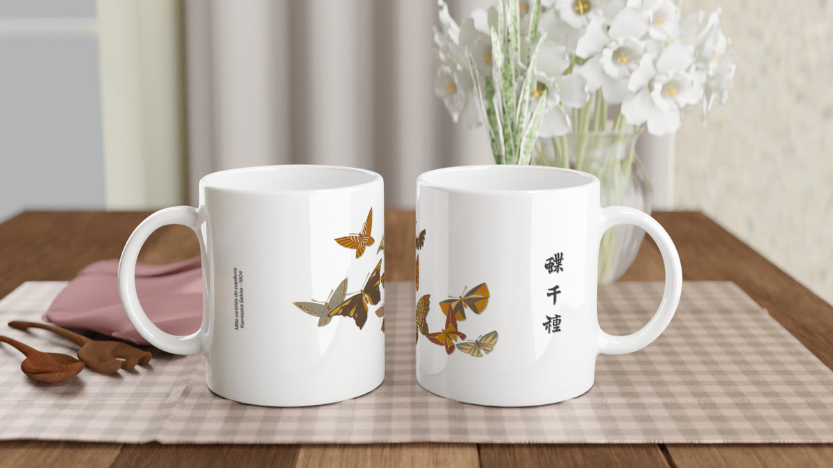 Becher mit herbstlichen Schmetterlingen von Kamisaka Sekka. Weißer Keramikbecher, illustriert mit einer künstlerischen Komposition aus Schmetterlingen mit grafischen Mustern in herbstlichen Ocker-, Orange- und Brauntönen, begleitet von vertikalen japanischen Kalligraphien.